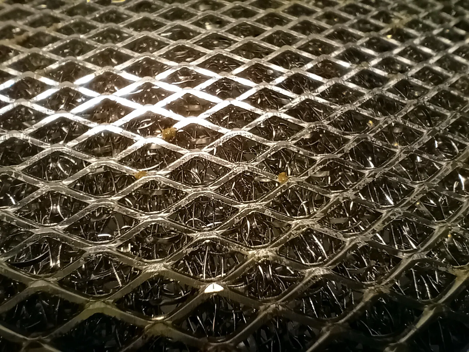 Close-up of an aluminum kitchen hood filter after being cleaned in a dishwasher on a 68-degree Celcius cycle.