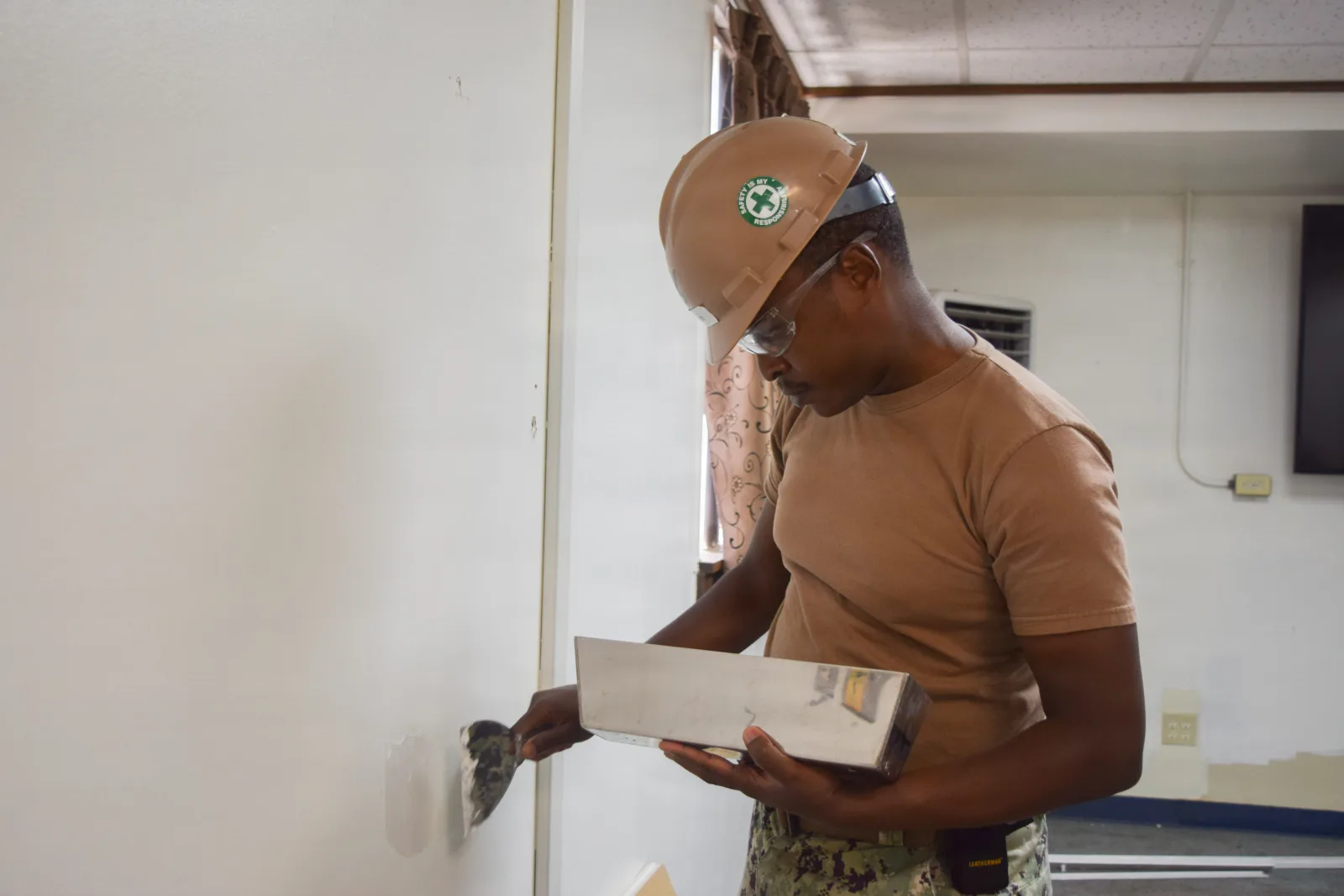 Construction Mechanic 2nd Class Moses Ondieki, assigned to Naval Mobile Construction Battalion (NMCB) 4, applies joint compound to patch drywall during office renovations at Osan Airforce Base, Osan, South Korea, on September 15, 2025. NMCB 4 is forward deployed throughout the Indo-Pacific region to support and maintain a free and open Indo-Pacific. As the stand-in, crisis response, naval engineering force, NMCB 4 maintains a ready posture to deliver in-theater expeditionary logistics via expeditionary shore infrastructure, forward damage repair, and mobile construction. (US Navy Photo by Builder 3rd Class Valera Cecan)