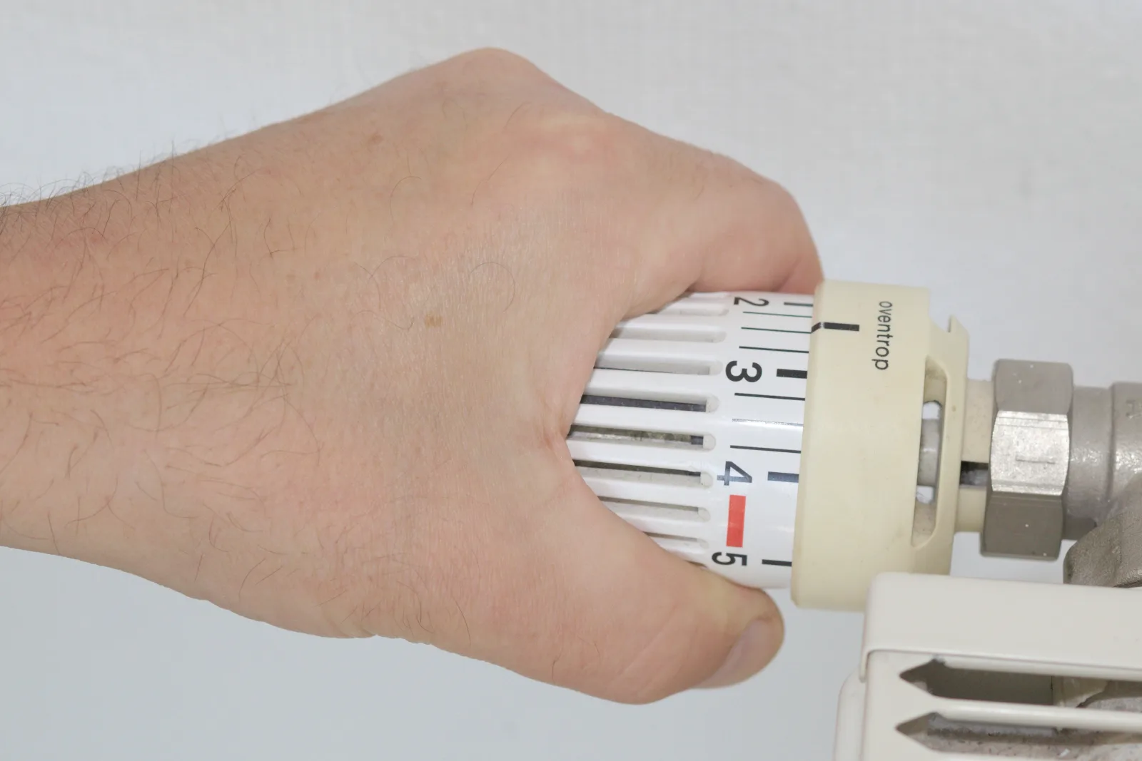 A hand is turning a thermostat on a radiator.