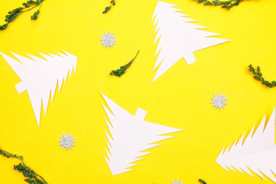 Stylish minimalist Christmas scene with paper trees and decorations on a vibrant yellow background.
