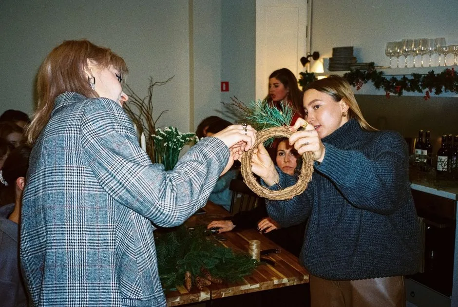 A group of women creating festive Christmas wreaths in a cozy indoor setting filled with decorations.