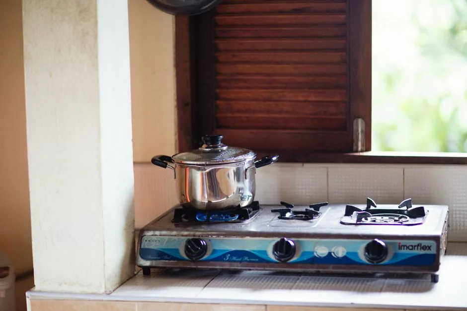 A stainless steel pot on a lit gas stove, next to a wooden shutter window.