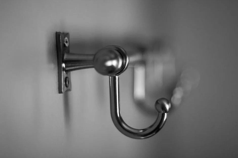 Detailed black and white close-up of a metallic hook on a wall, showcasing texture.