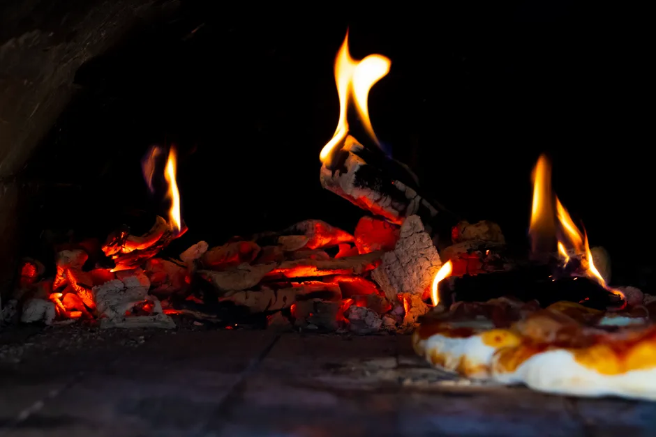 A close-up of a stone oven with bright flames, showcasing the baking process of a pizza.