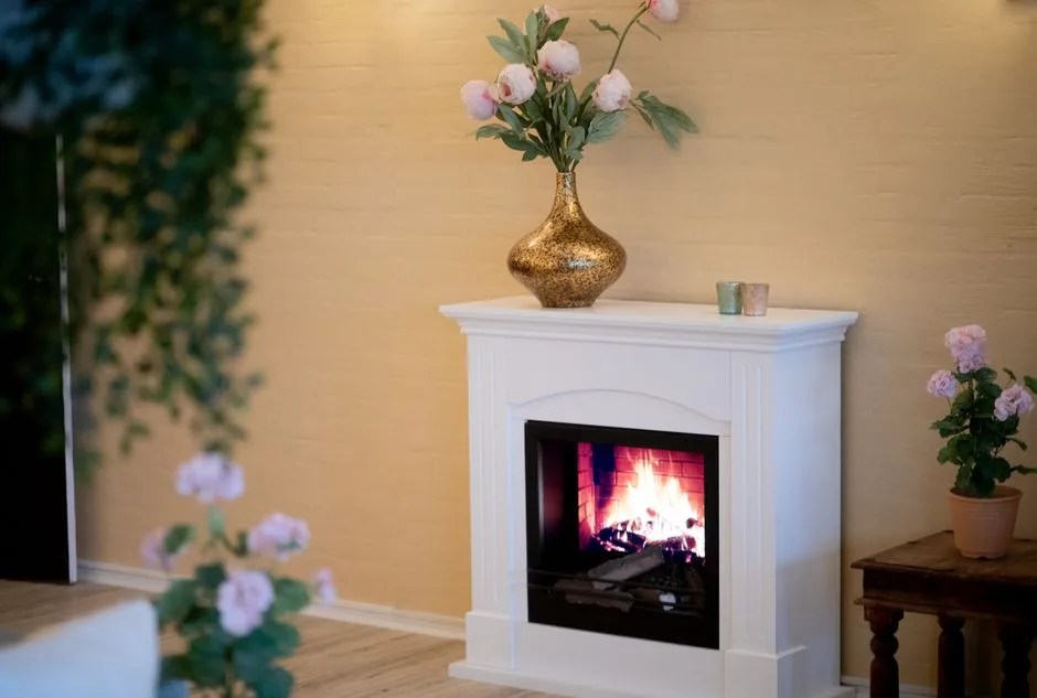 Warm living room with a lit fireplace, elegant vase with flowers, and cozy ambiance.