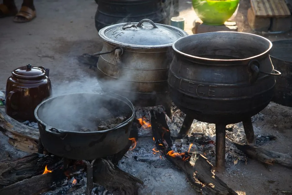 Traditional outdoor cooking with cast iron pots and open fire.
