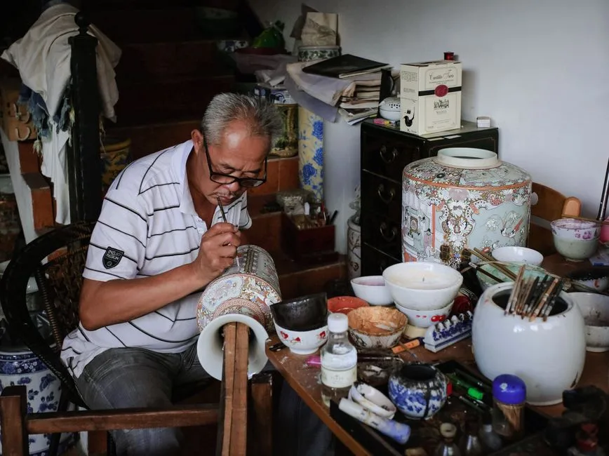 An artisan skillfully painting patterns on a ceramic vase in a traditional workshop setting.