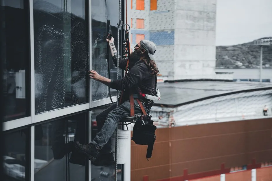 A man cleaning skyscraper windows with a harness, showcasing urban high-rise work.
