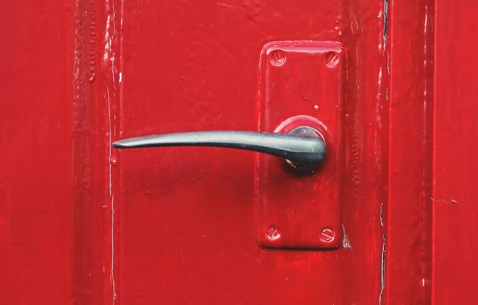 Close-up of a bright red painted door with a metallic handle.