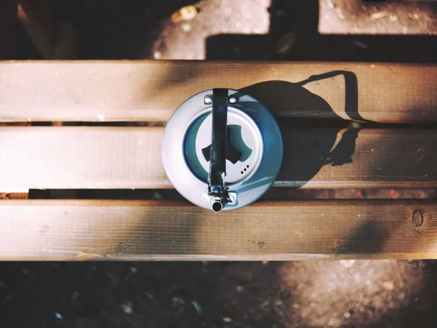Overhead shot of a vintage kettle on a wooden bench outdoors, casting a shadow.