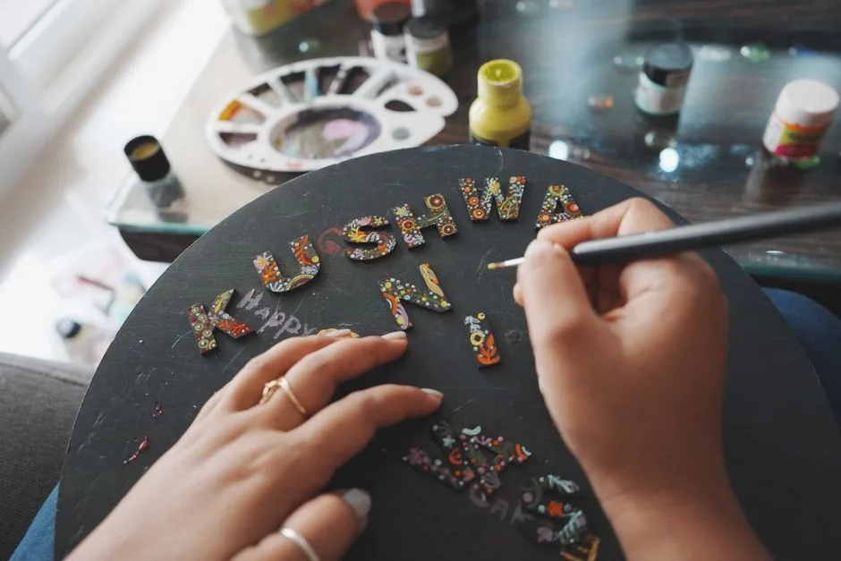 Close-up of a hand painting decorative letters with intricate designs on a board.
