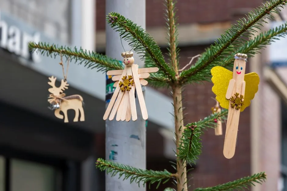 Colorful handmade Christmas ornaments on a pine tree branch outdoors, creating a festive holiday vibe.