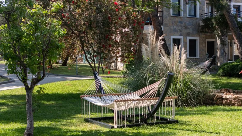 A tranquil garden with a hammock surrounded by lush greenery and blooming trees in Bodrum, Turkey.