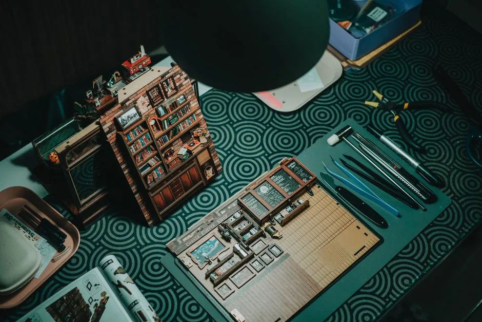 A detailed miniature bookshelf crafting setup with tools on a patterned table.