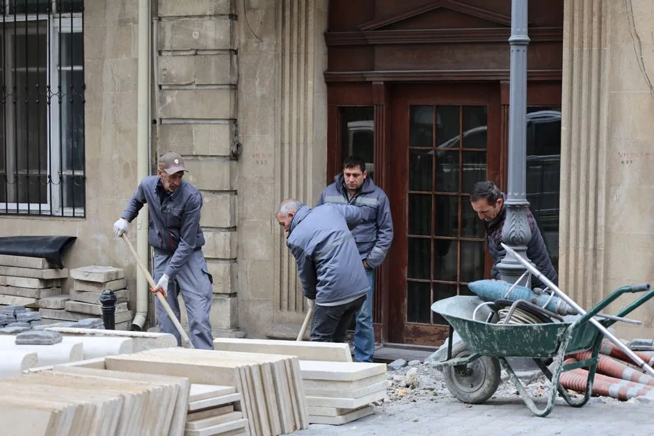 Team of men working on paving new city sidewalk with stones. Urban construction scene with workers.