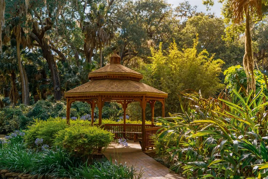 A beautiful wooden gazebo surrounded by lush greenery and vibrant plants in a sunlit garden.
