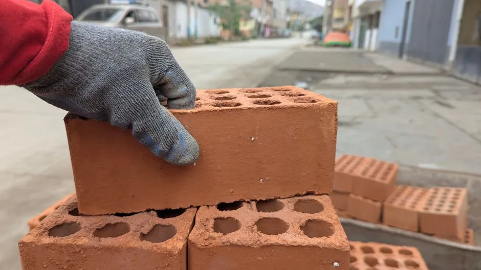 A worker with a glove stacking bricks on a street construction site.