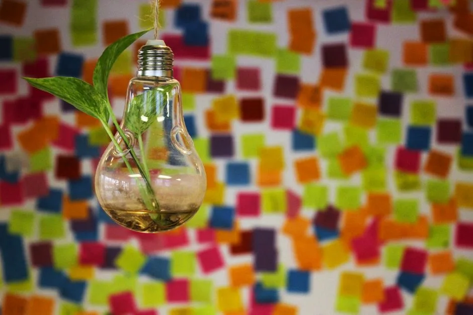Hanging light bulb vase with greenery against colorful post-it notes.