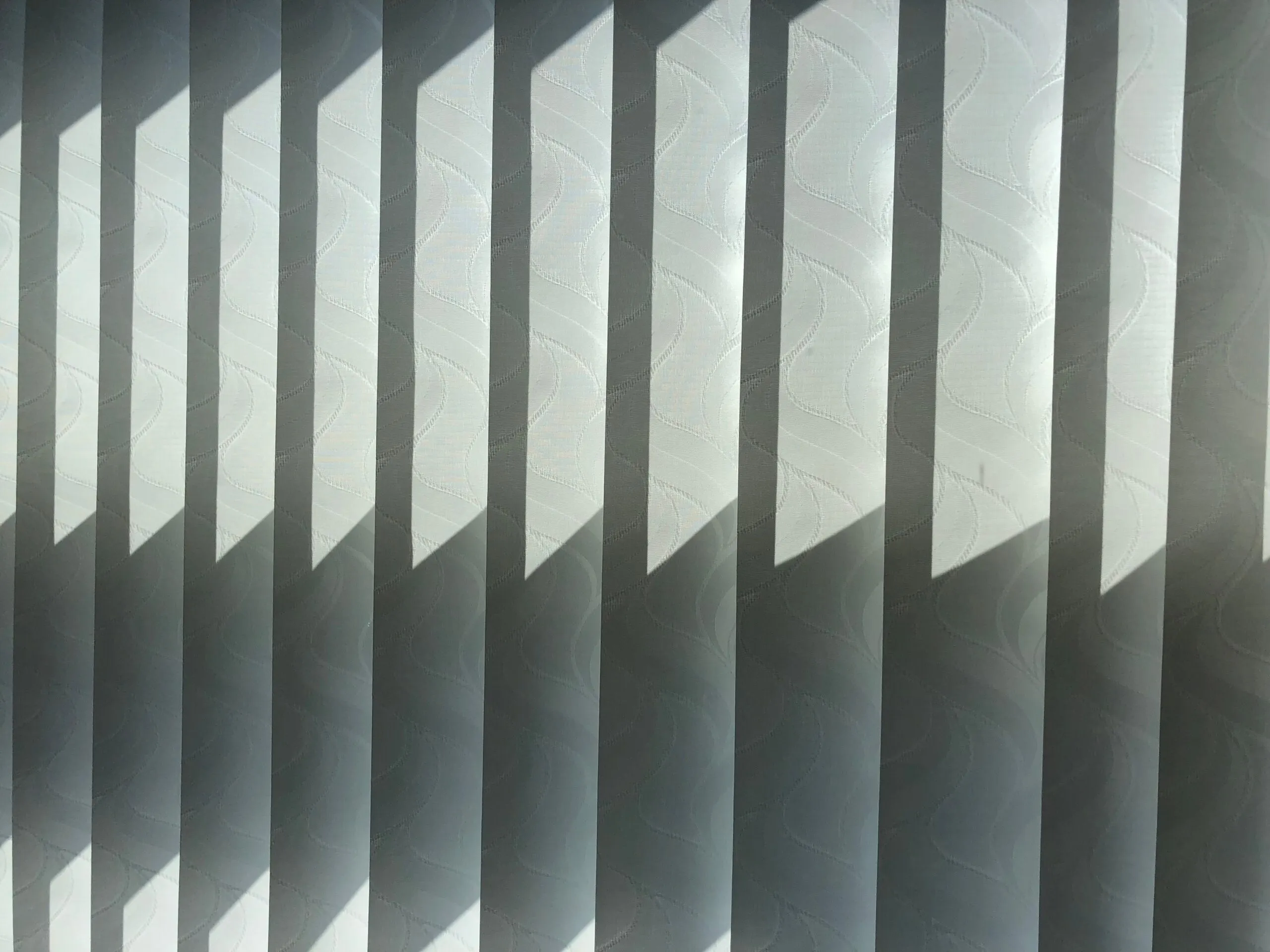 Vertical simple white textile window blinds hanging in room in sunlight as abstract background