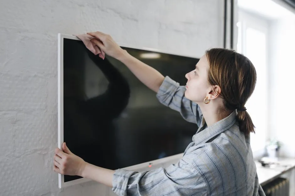 Woman wiping flat screen TV indoors, focusing on cleaning and maintenance.