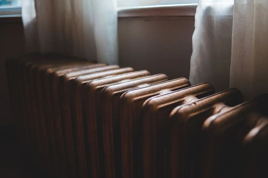 Aged heating battery made of cast iron near windowsill with curtains in house