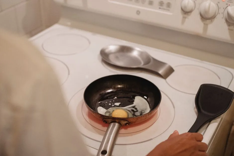 Crop anonymous person with black spatula near white stove cooking fried eggs in kitchen
