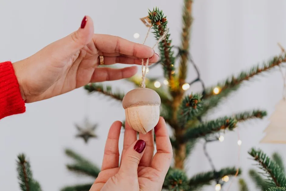 Close-up of hands hanging an acorn ornament on a decorated Christmas tree.