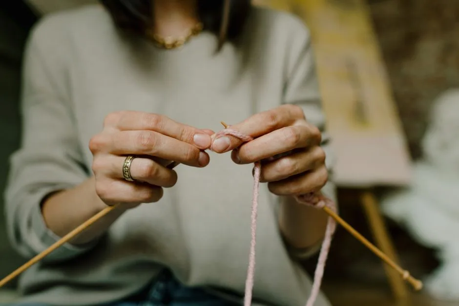 A close-up shot of hands knitting with pink yarn, showcasing detailed craftsmanship.