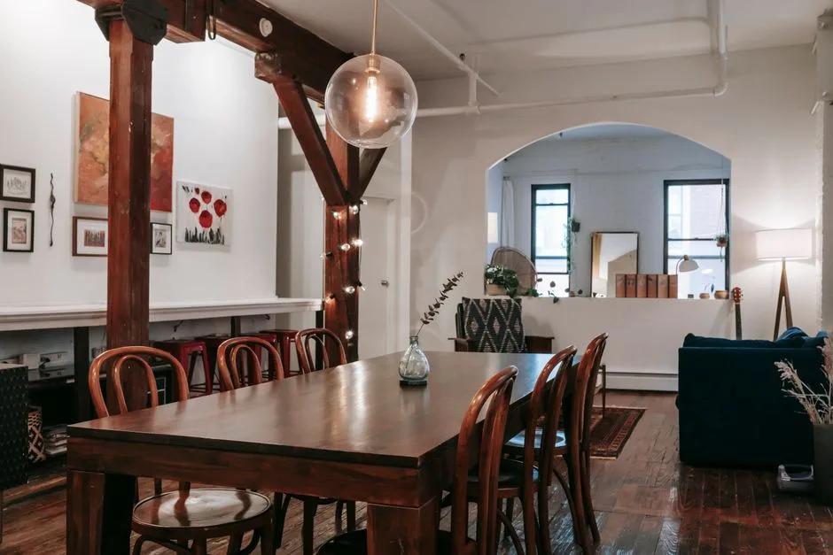 Interior of wooden table with glowing lamps hanging on pillar in creative light living room with furniture and arched aperture