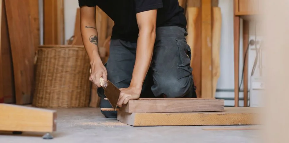 Crop anonymous male with tattoo sawing piece of timber detail with planer in workshop