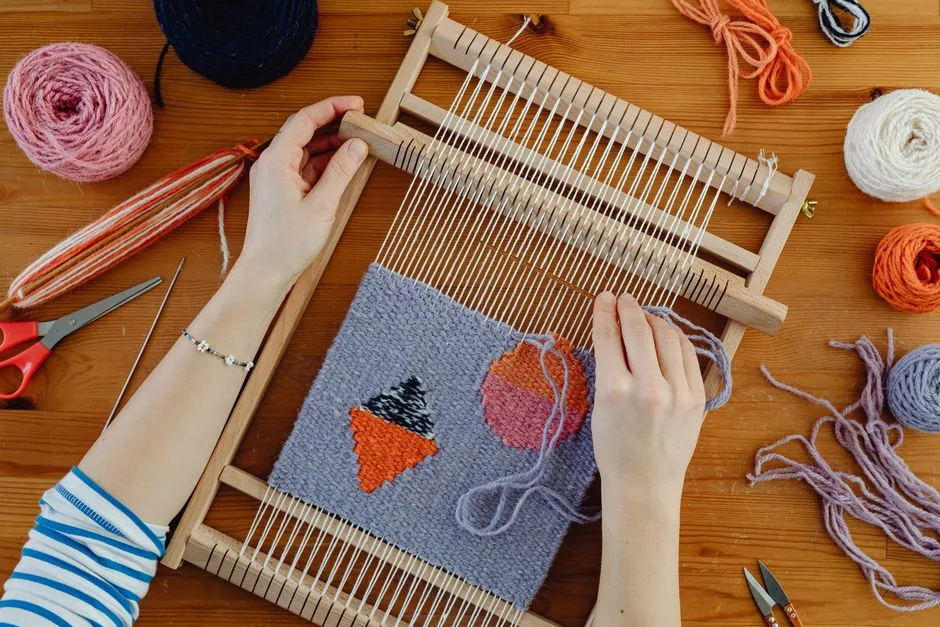 Close-up of hands weaving colorful patterns using a loom and yarn on wooden surface.