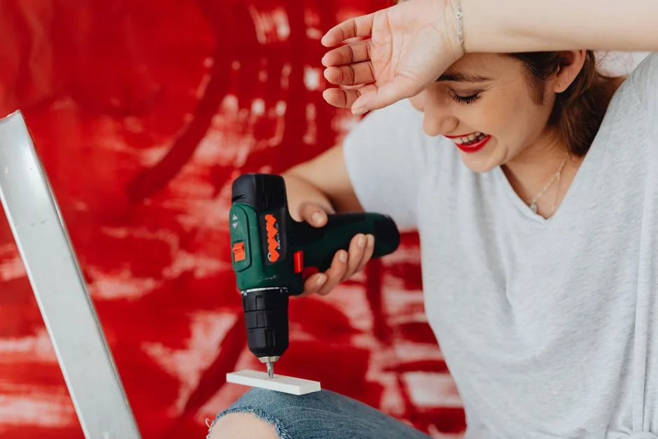 A joyful woman uses a power drill against a red background. DIY concept.
