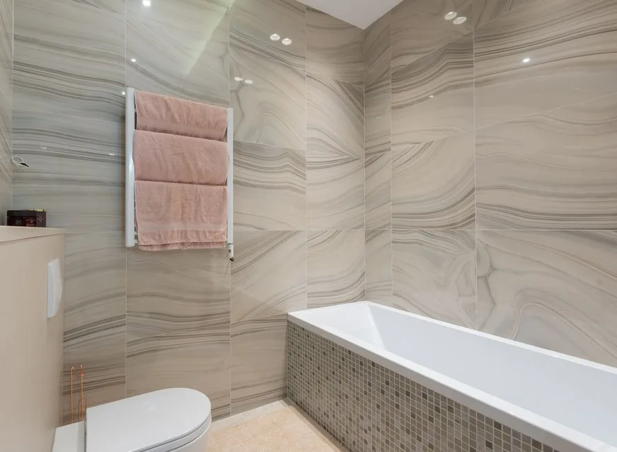 Contemporary bathroom interior with toilet bowl against bathtub and tiled walls with towels on rack in light house
