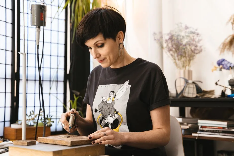 Focused woman using tools in a cozy artisan studio to create handmade jewelry.