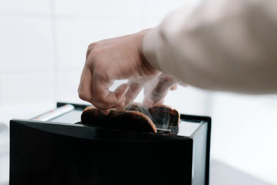 A hand carefully extracts hot toast from a toaster, with steam visible.