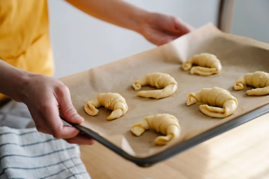 Person holding a baking sheet with raw croissants on parchment paper.