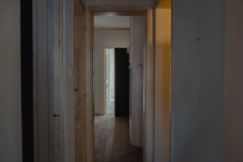 A dimly lit hallway in an apartment with wooden doors and a rustic feel.