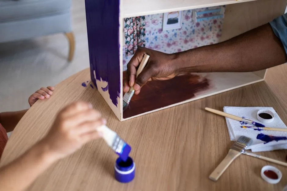 Adults and child creatively painting a wooden dollhouse using vibrant colors and brushes.