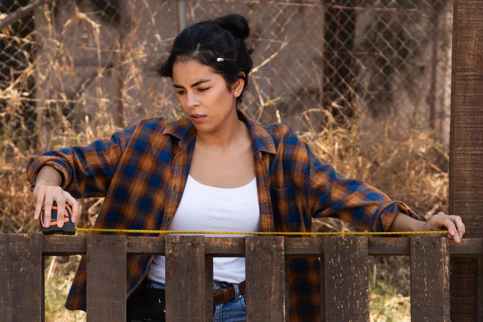 Focused woman using measuring tape on fence, showcasing empowerment in carpentry.