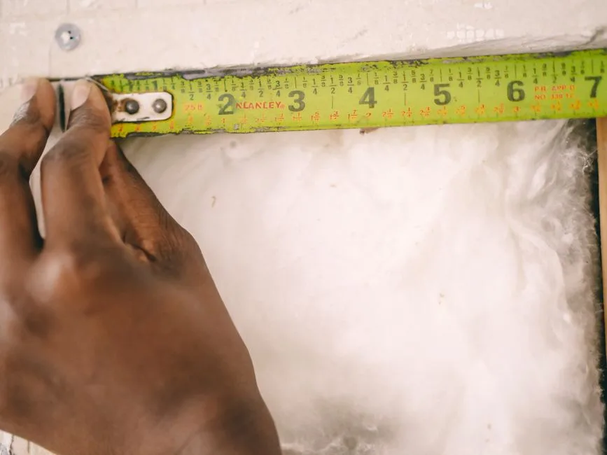 Close-up of a hand measuring insulation with a yellow tape measure.