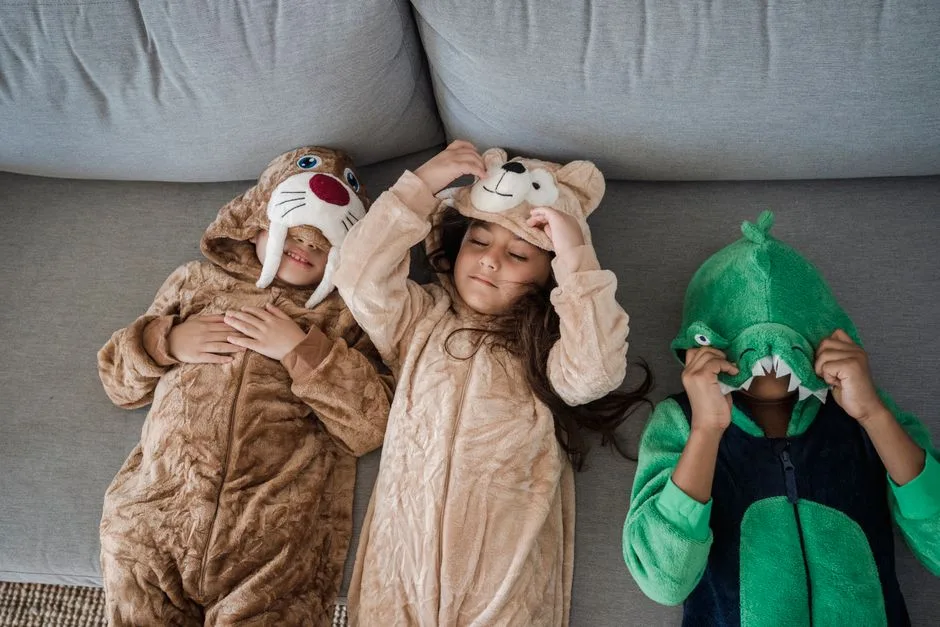 Three kids wearing animal costumes playing together on a sofa, enjoying fun and laughter.