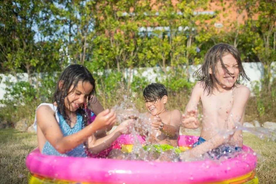 Three children enjoying a sunny day splashing in an inflatable pool outdoors.