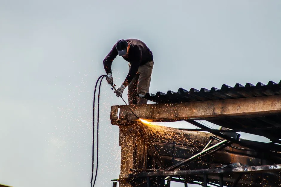 A worker cutting metal on a roof with visible sparks during construction work.