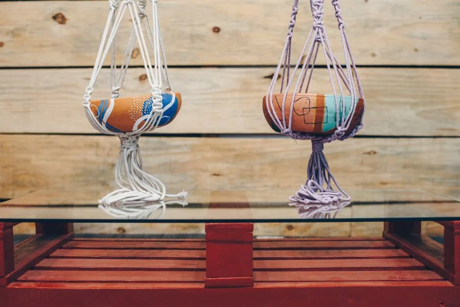 Two colorful bowls suspended by macrame strings on a wooden table with a rustic background.
