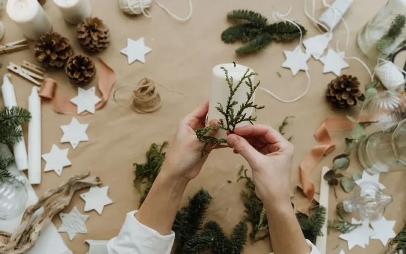 Hands decorating a candle with greenery for a cozy winter holiday setting.