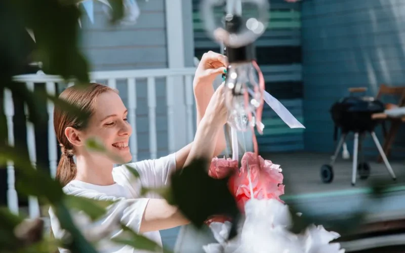 Smiling woman decorates with paper pom-poms for an outdoor party.