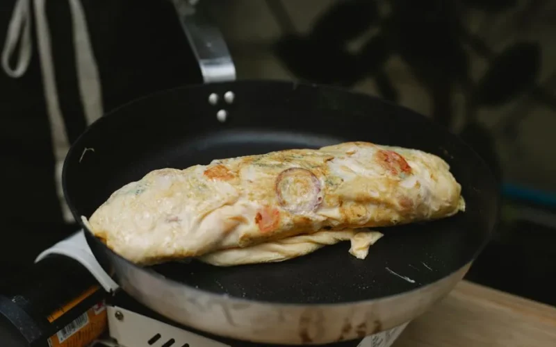 Yummy fresh omelette roll with tomatoes and radish frying on pan in kitchen