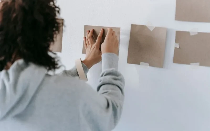 A woman creatively arranging blank cards on the wall to enhance home decor.