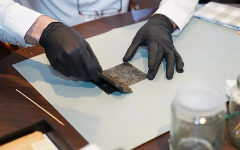 A restorer carefully working on a photograph with gloves and brush, focusing on details.