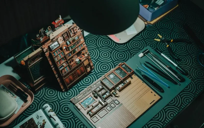 A detailed miniature bookshelf crafting setup with tools on a patterned table.
